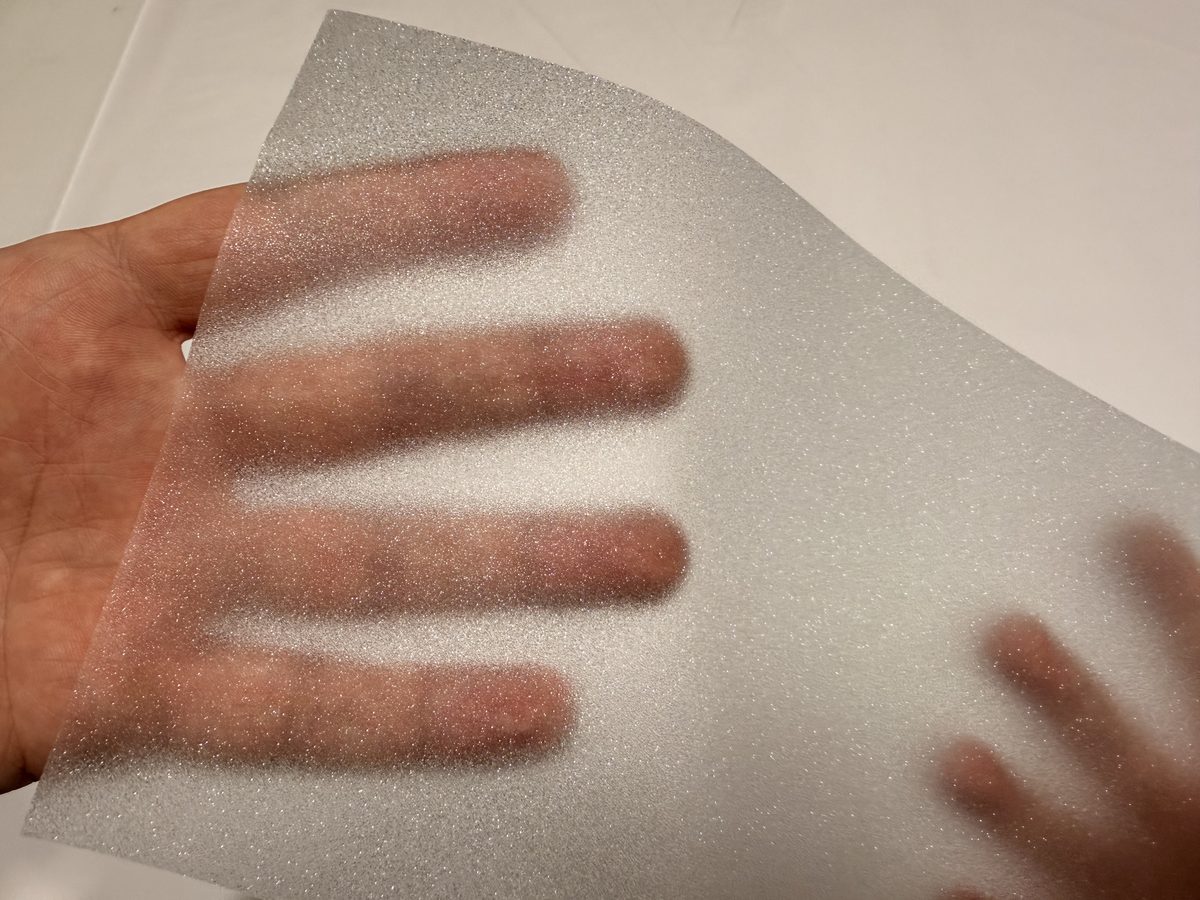 A hand behind a piece of frosted film shows only as a soft blur.