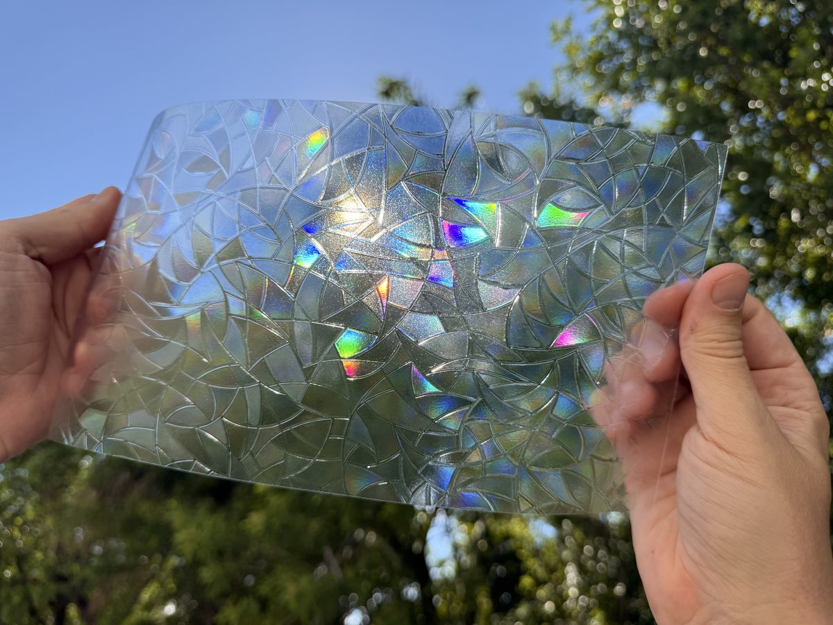 A piece of rainbow film held up to the sun, with small rainbow flecks in the mosaic.