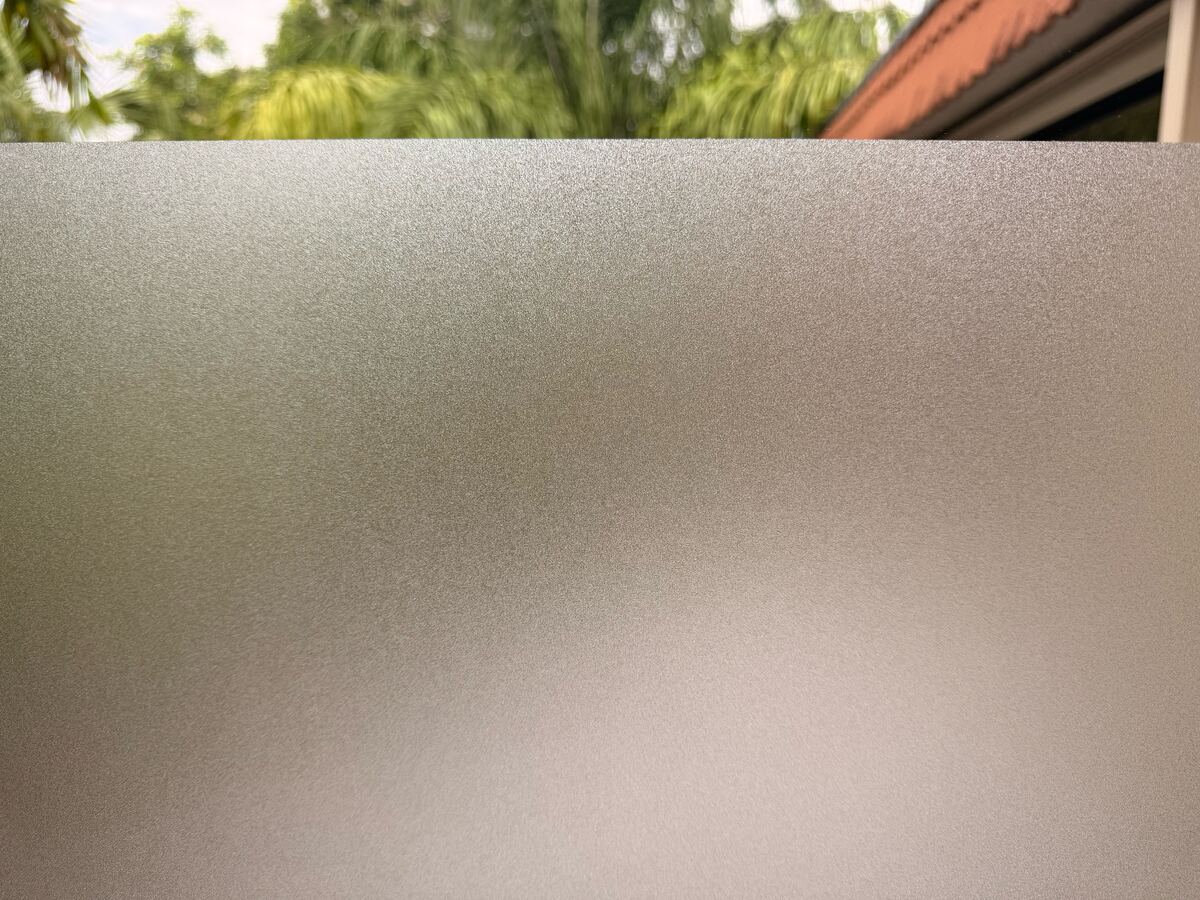 A window with SHINECOR frosted film on the lower glass: palm trees and a roof are clear above it and blurred behind it.