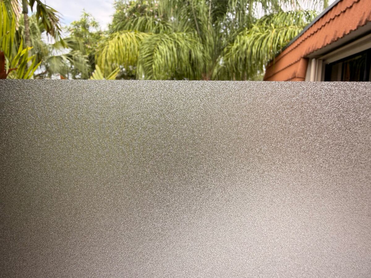 Frosted film covering the lower part of a window, with trees and a red roof visible through the clear glass above.