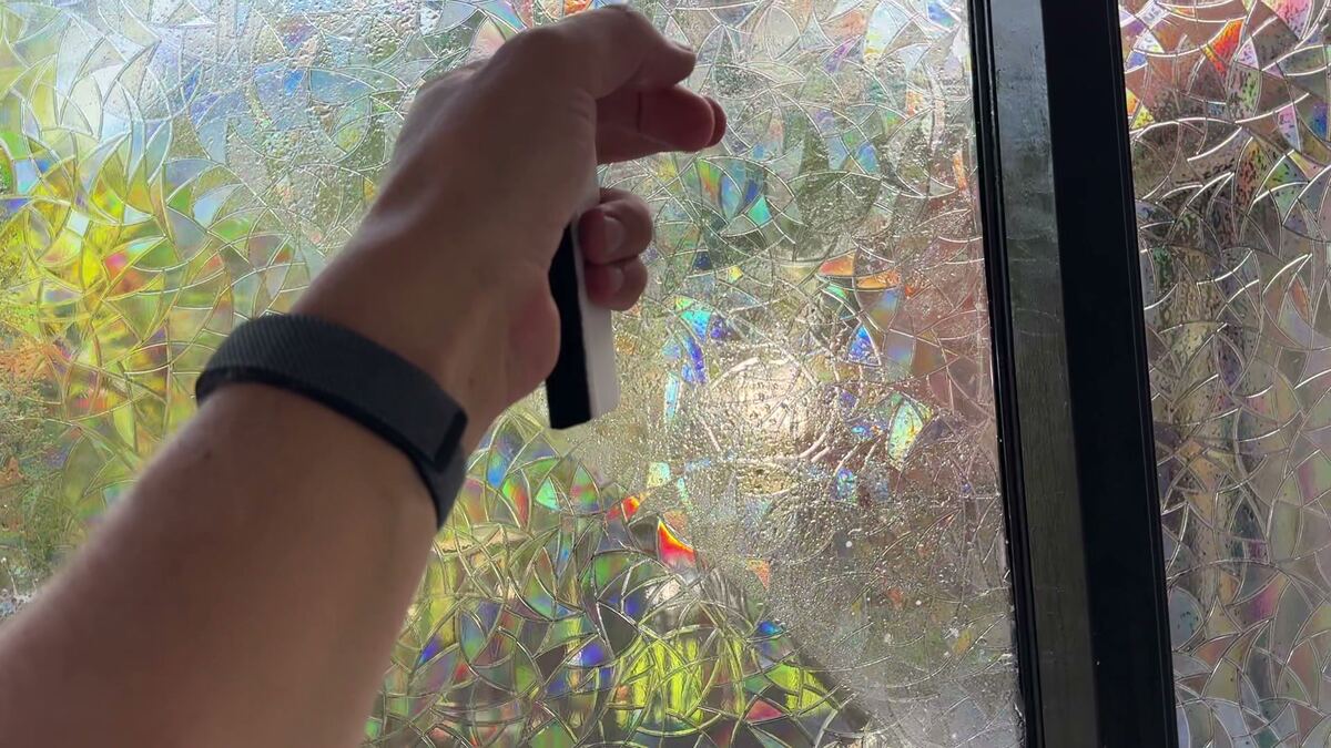 A hand smoothing freshly placed rainbow film on wet glass.