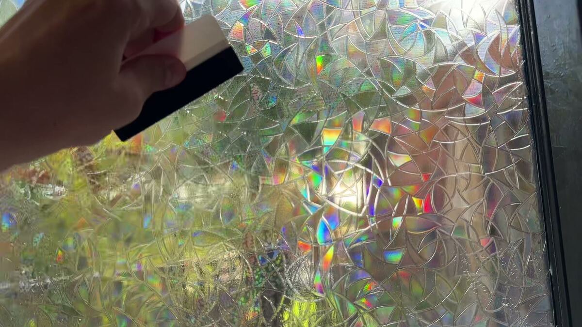 A hand pressing window film onto wet glass with a squeegee.